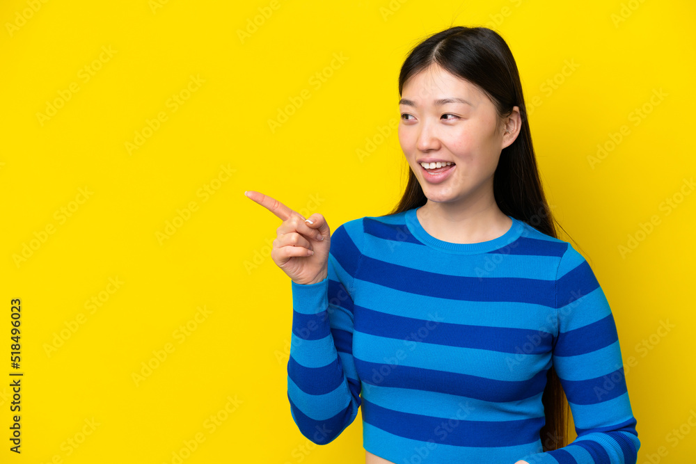 Young Chinese woman isolated on yellow background pointing finger to the side and presenting a product Young Chinese woman isolated on yellow background pointing finger to the side and presenting a product