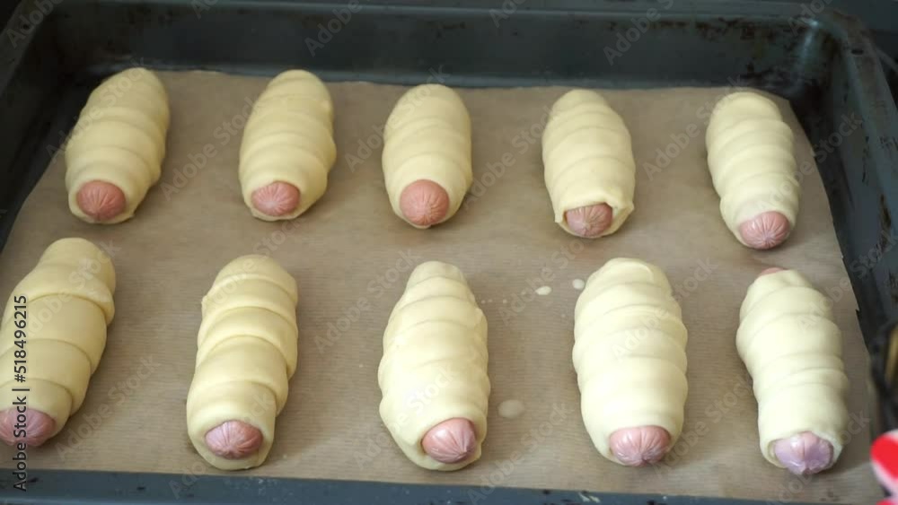 Female hand smearing sausages in dough with beaten eggs