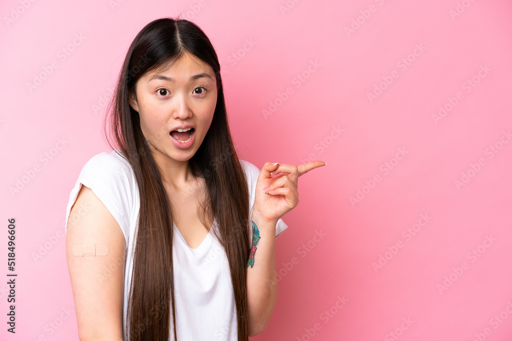 Young Chinese woman wearing a band aids isolated on pink background surprised and pointing finger to the side Young Chinese woman wearing a band aids isolated on pink background surprised and pointing finger to the side