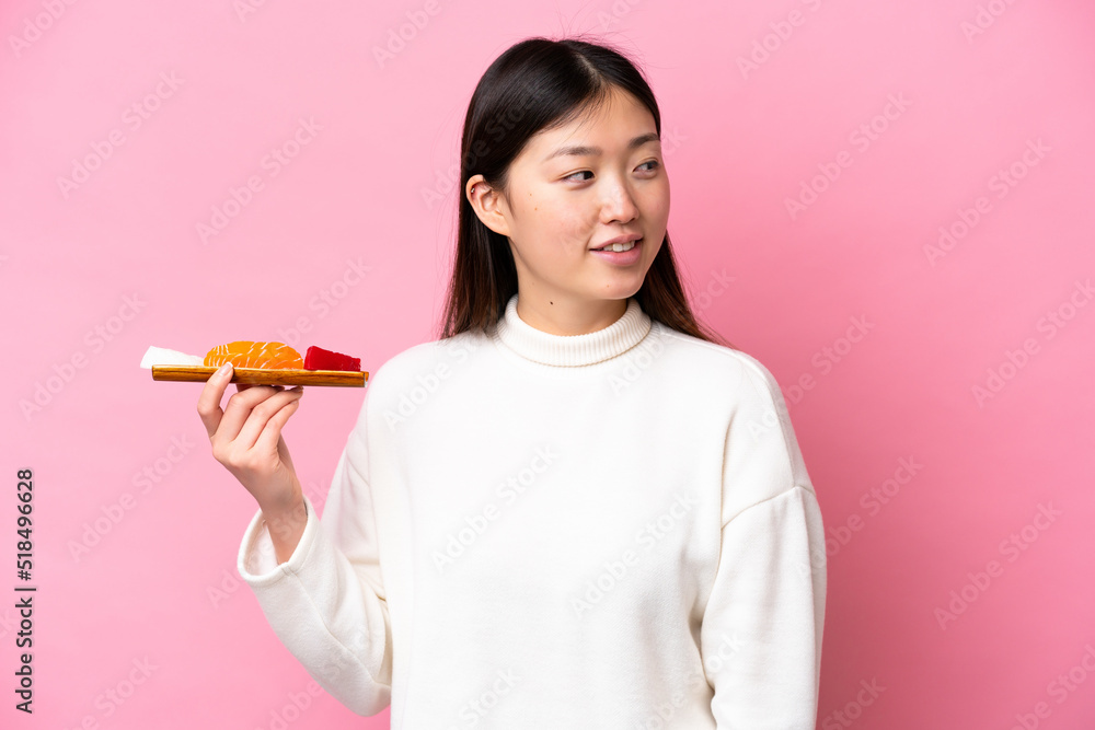 Young Chinese woman holding sashimi isolated on pink background looking to the side and smiling Young Chinese woman holding sashimi isolated on pink background looking to the side and smiling