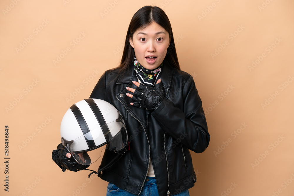 Young Chinese woman with a motorcycle helmet isolated on beige background surprised and shocked while looking right