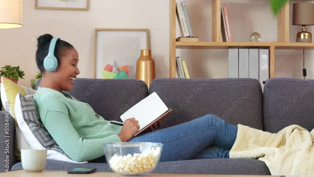 Black student streaming an audio book while making notes in a diary and relaxing on a couch. Young African American making a list of creative ideas while enjoying an online podcast in a living room Black student streaming an audio book while making notes in a diary and relaxing on a couch. Young African American making a list of creative ideas while enjoying an online podcast in a living room