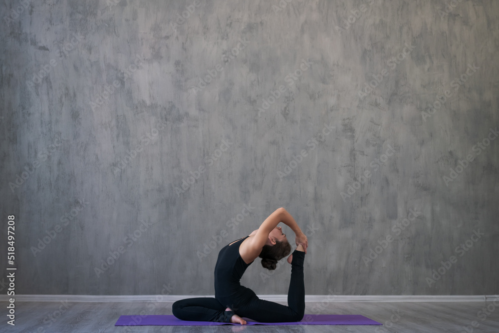 Young attractive caucasian woman doing yoga, sitting in workout yoga pose, wearing sportswear full length indoors, against gray wall. The concept of a healthy lifestyle and longevity