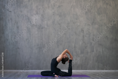 Fototapeta Naklejka Na Ścianę i Meble -  Young attractive caucasian woman doing yoga, sitting in workout yoga pose, wearing sportswear full length indoors, against gray wall. The concept of a healthy lifestyle and longevity