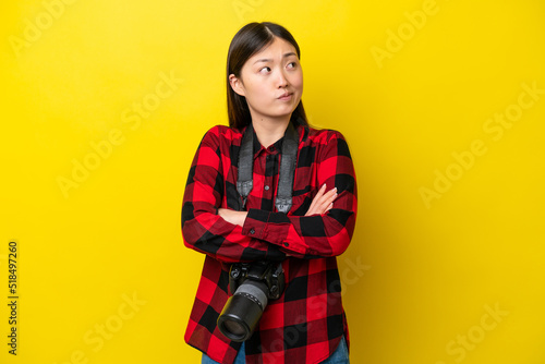 Young photographer Chinese woman isolated on yellow background making doubts gesture while lifting the shoulders © luismolinero