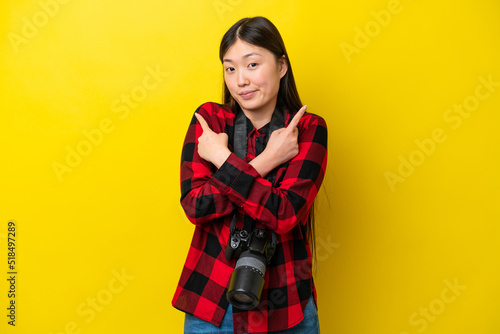 Young photographer Chinese woman isolated on yellow background pointing to the laterals having doubts © luismolinero