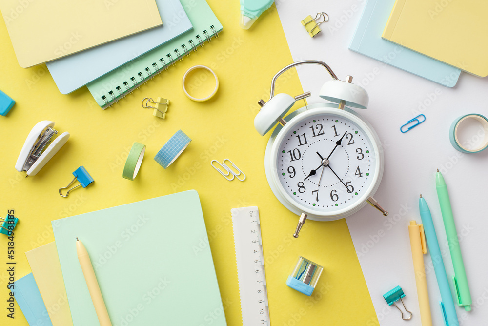 Back to school concept. Top view photo of alarm clock diaries sharpener ruler pens binder clips adhesive tape and stapler on bicolor yellow and white background Back to school concept. Top view photo of alarm clock diaries sharpener ruler pens binder clips adhesive tape and stapler on bicolor yellow and white background