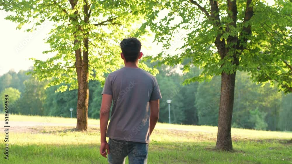 Back view of a young man casually taking a stroll over the lush green grasses of beautiful park. Back view of a young man casually taking a stroll over the lush green grasses of beautiful park.