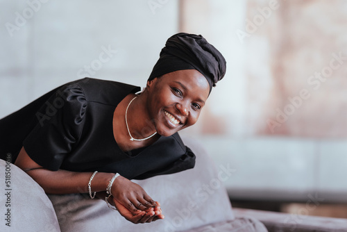 Photography Cheerful African young adult woman black turban and black dress leaning on cushion looking at camera smiling wide with copy space on background