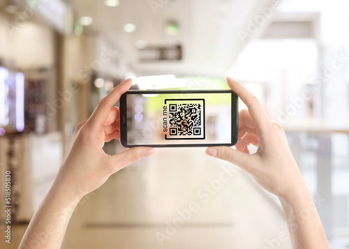 Woman holding smartphone with QR code on screen in store, closeup
