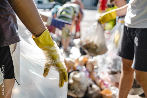 People in yellow gloves sort plastic from a bin into a transparent bag for recycling to reduce plastic waste