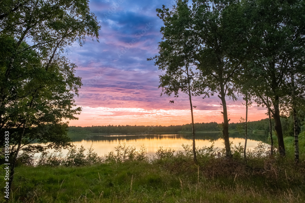 a beautiful blue lake with some tree silhouettes in the foreground under a dramatic sunset sky. High quality photo