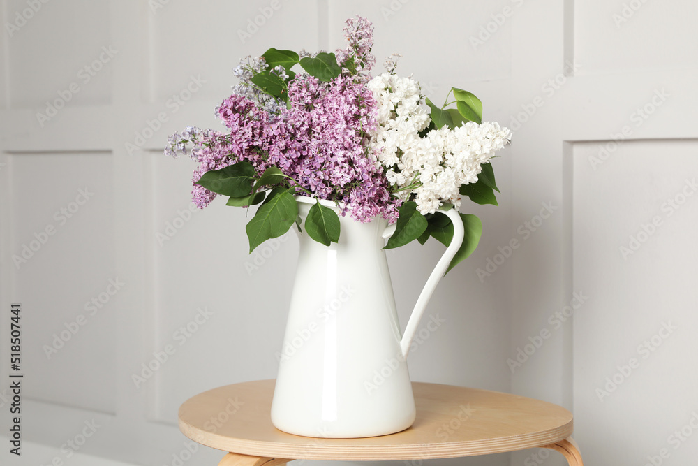 Fototapeta premium Beautiful lilac flowers in vase on wooden table near white wall