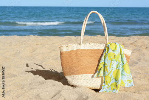 Straw bag with beach wrap on sandy seashore  space for text. Summer accessories