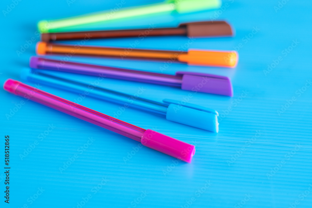 Fototapeta premium Side view of selective focus shot of color pens lying on blue background. 