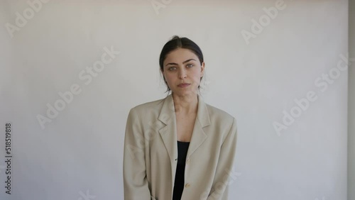 Young beautiful confident successful startup woman with dark hair take professional photo studio portrait. Female model unbutton jacket, sit, pose, look at camera on white background. Business concept