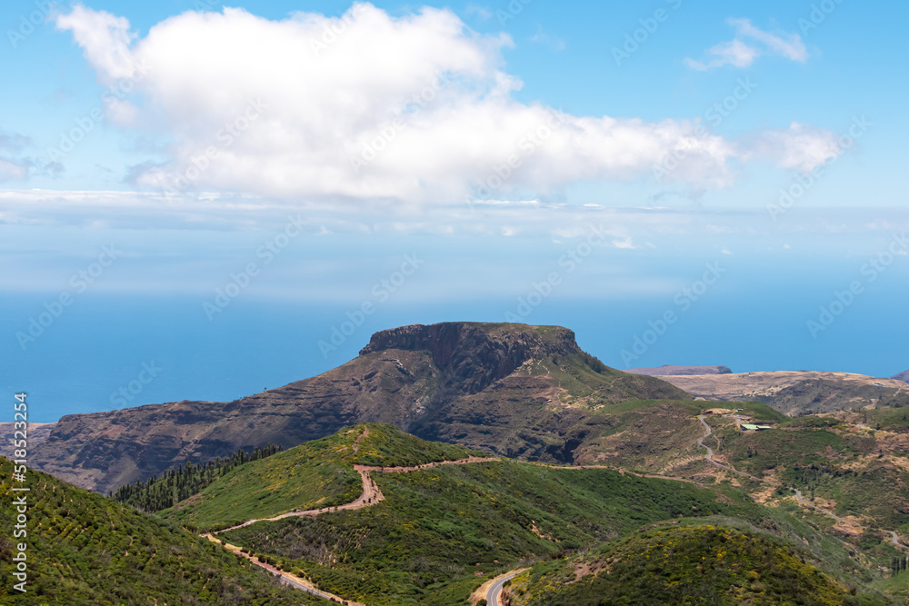 Fototapeta premium Panoramic view on massive volcanic plug Fortaleza de Chipude overlooking western coast of La Gomera, Canary Islands, Spain, Europe. Atlantic Ocean in background. Hilly mountain road to Valle Gran Rey