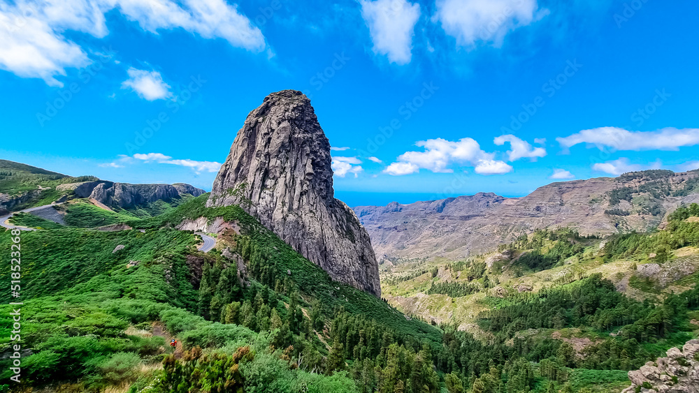Scenic mountain road with view on massive volcanic rock formation Roque de Agando in Garajonay National Park on La Gomera, Canary Islands, Spain, Europe. Lava cone of old volcano. Sunny day in summer