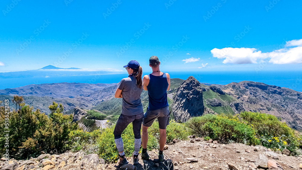 Couple with scenic view on mountain road next to volcanic rock formation Roque de Agando in Garajonay National Park, La Gomera, Canary Islands, Spain, Europe. Seen from lookout Mirador Morro de Agando