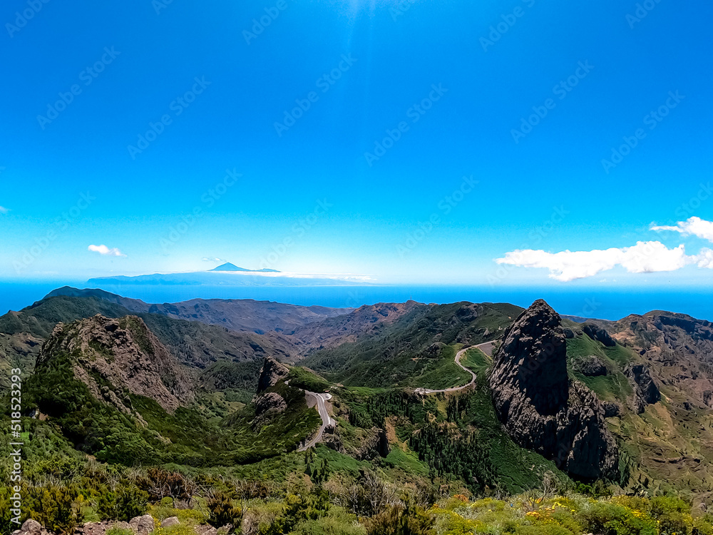 Obraz premium Scenic mountain road with view on massive volcanic rock formation Roque de Agando in Garajonay National Park on La Gomera, Canary Islands, Spain, Europe. View seen from lookout Mirador Morro de Agando