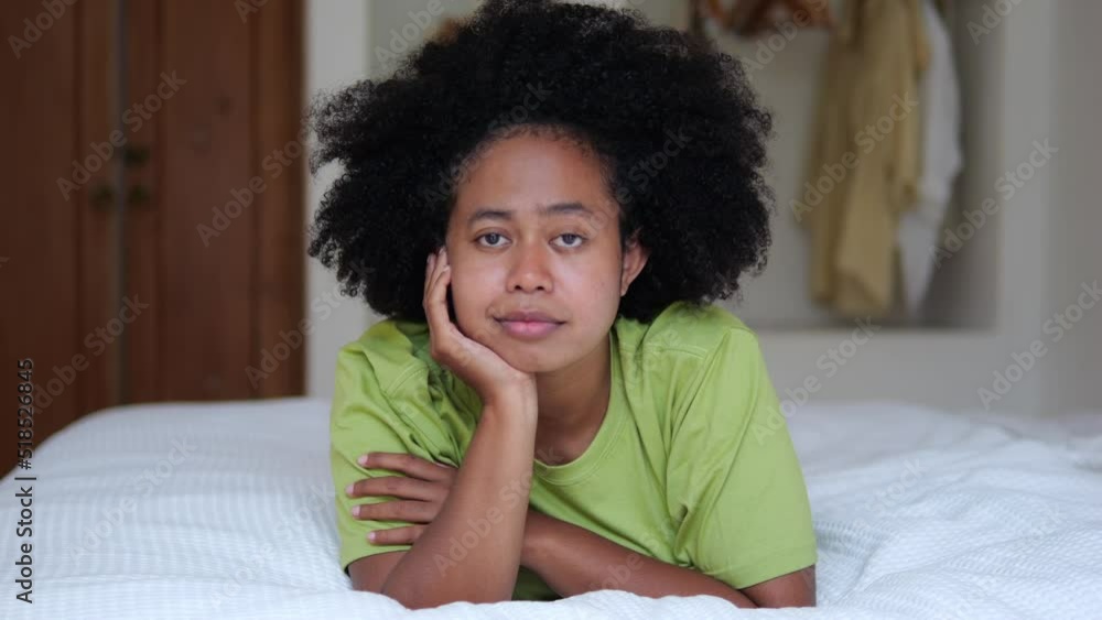 Close-up happy afro asian woman with afro hairstyle lies on the bed in the hotel in quarantine. Portrait in the bedroom on the bed in the hotel, happy to spend time in quarantine during the pandemic. Close-up happy afro asian woman with afro hairstyle lies on the bed in the hotel in quarantine. Portrait in the bedroom on the bed in the hotel, happy to spend time in quarantine during the pandemic.