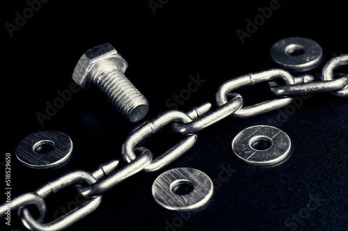 A metal chain lies on a black background, next to it are washers and a thick bolt, a still life of fasteners