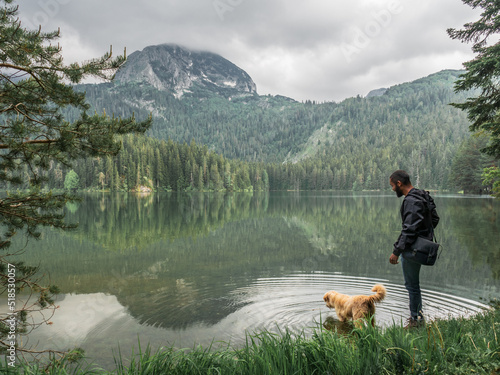 Homem negro com cachorro ao lado e com paisagem com lago e montanhas em Montenegro