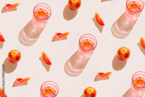 Creative pattern made of bloody orange and glass of fresh cocktail or lemonade on pastel beige backgound. Summer refreshment concept. Sunlit flat lay. Minimal style. Top view