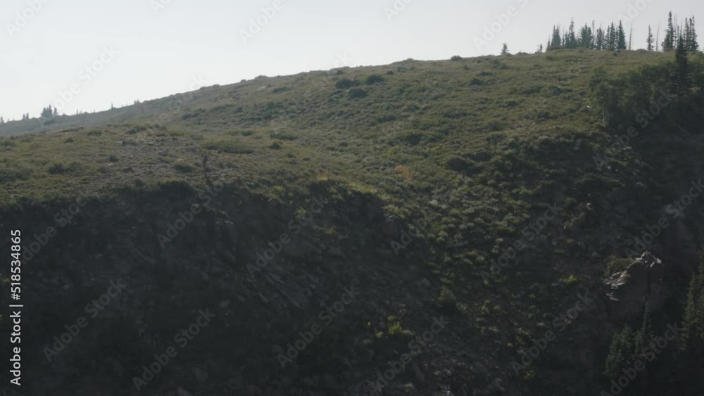 Drone shot of guy hiking in Utah mountains. Hiking across mountain top. Hiking trail drone shots. Man hunting on top of a ridge. Ridge line with a man on it in the distance. Rocky Mountains in summer. Drone shot of guy hiking in Utah mountains. Hiking across mountain top. Hiking trail drone shots. Man hunting on top of a ridge. Ridge line with a man on it in the distance. Rocky Mountains in summer.