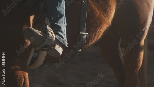 Boot in stirrup. Cowboy boot in saddle. Boots and spurs close up. Barrel racing on a horse. Riding on a horse in arena. Western clothing and a horse.