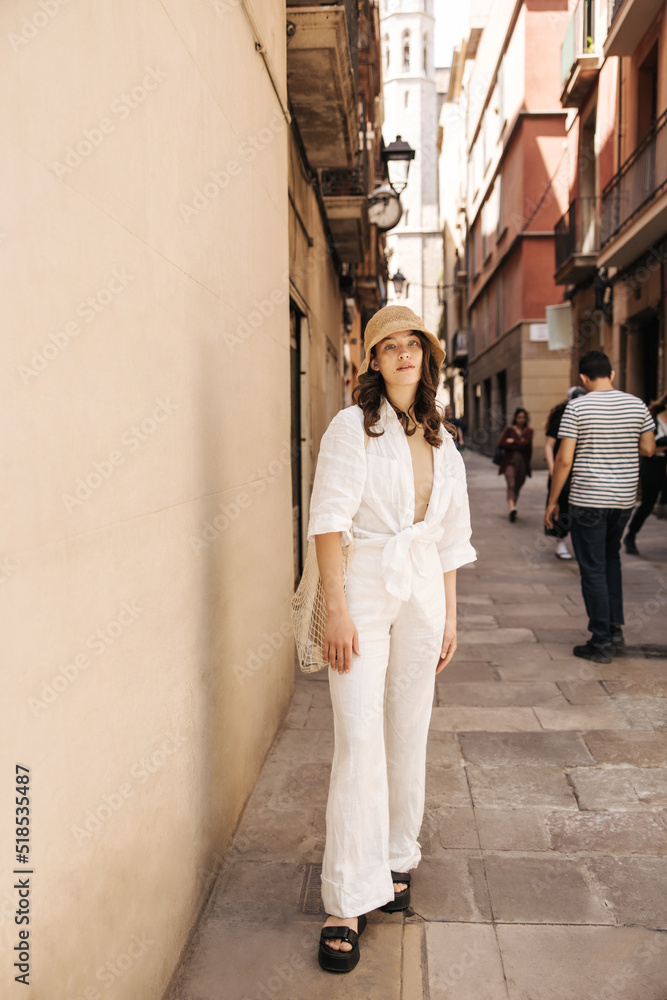 Full length stylish young caucasian woman posing looking at camera relaxing in city center. Brunette wears panama, shirt and pants spring. Relaxation concept