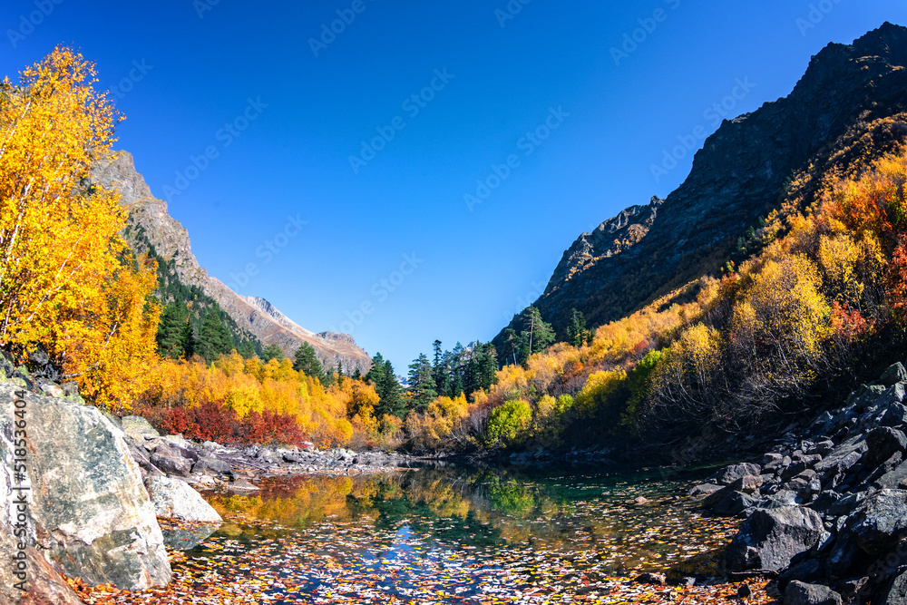 Beautiful autumn landscape with clear green water of a mountain lake and trees with autumn foliage reflected in it