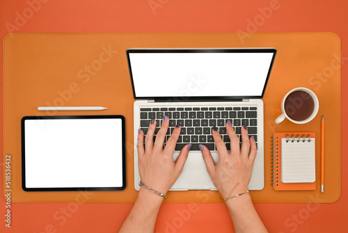 Top view of man's hands painted nails using Empty white screen of laptop and digital tablet on the orange background, Office desk and Copy space concept.