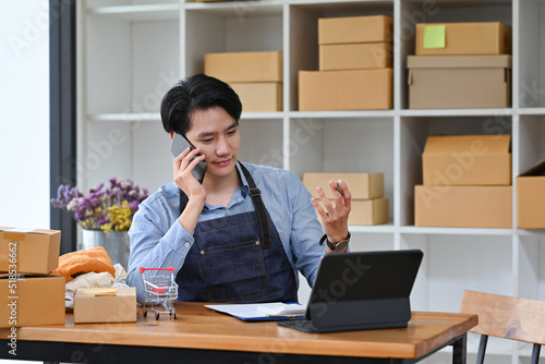 Young Asian man entrepreneur, Business owner using a smartphone and working with tablet, stock shelf as the background.