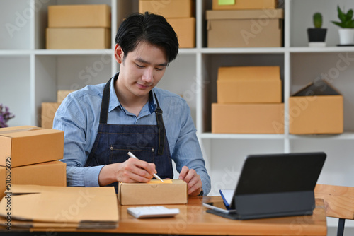 Young start up small business owner man writing address on cardboard box at workplace, Small business entrepreneur SME or Freelance asian man working with box, Shipping shopping online concept.