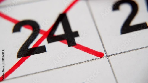 The 24st number in the calendar is crossed out with a red cross in a macro on a white sheet. Calendar for plans, notes, meetings. Business calendar. Marker for notes in the calendar photo