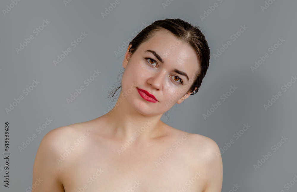 Portrait of a young woman on a gray background. Black hair is pulled back. Bare shoulders. Portrait of a young woman on a gray background. Black hair is pulled back. Bare shoulders.