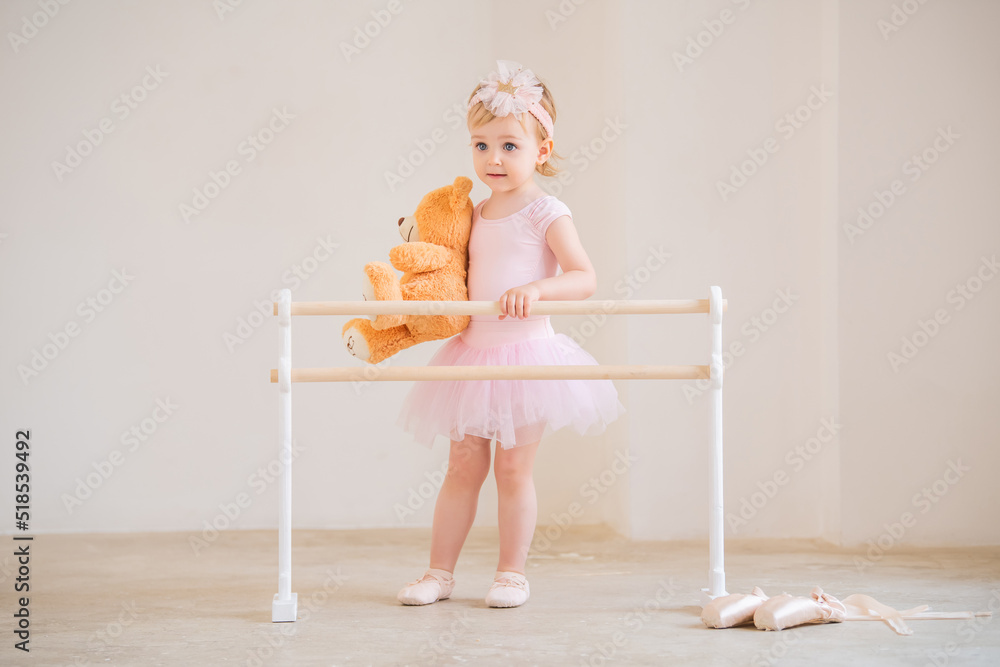 Cute blueeyed baby ballerina in pink, standing near the ballet barre
