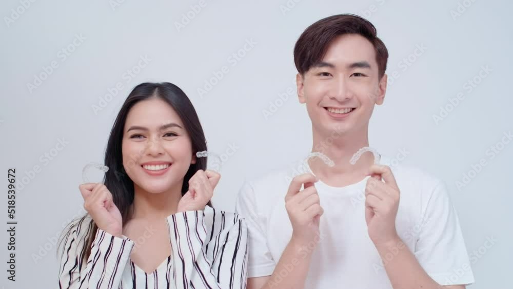 Young smiling man and woman holding invisalign braces over white background studio, dental healthcare and Orthodontic concept