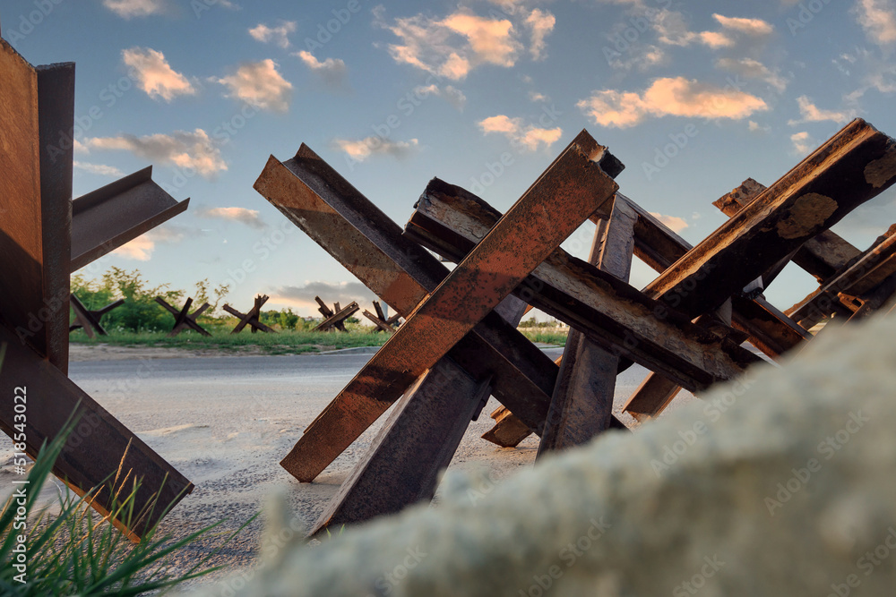 Rusty anti-tank hedgehogs on the wet grass on sunset background. War in Ukraine Rusty anti-tank hedgehogs on the wet grass on sunset background. War in Ukraine