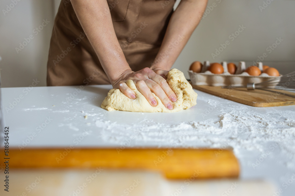 A woman in an apron prepares dough for baking at home. Rolling out and preparing dough for baking.