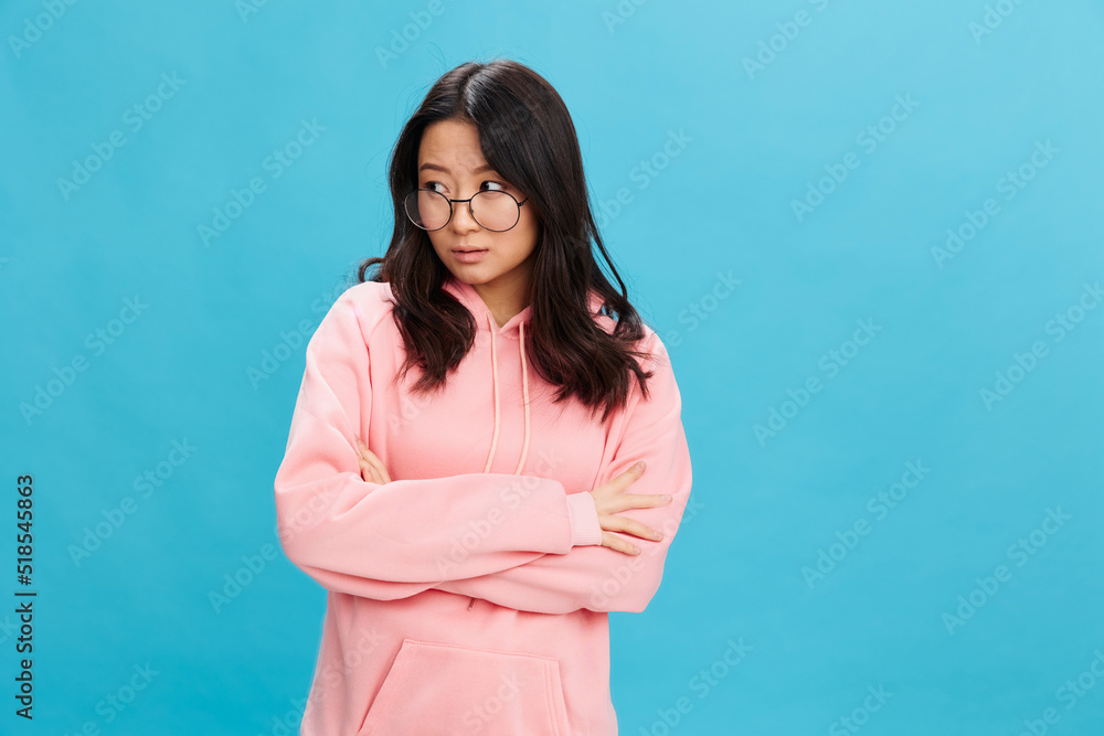 Upset cute Asian student young lady in pink hoodie sweatshirt wear round glasses cross hands posing isolated on blue studio background. The best offer for ad. Eyewear for vision correction concept Upset cute Asian student young lady in pink hoodie sweatshirt wear round glasses cross hands posing isolated on blue studio background. The best offer for ad. Eyewear for vision correction concept