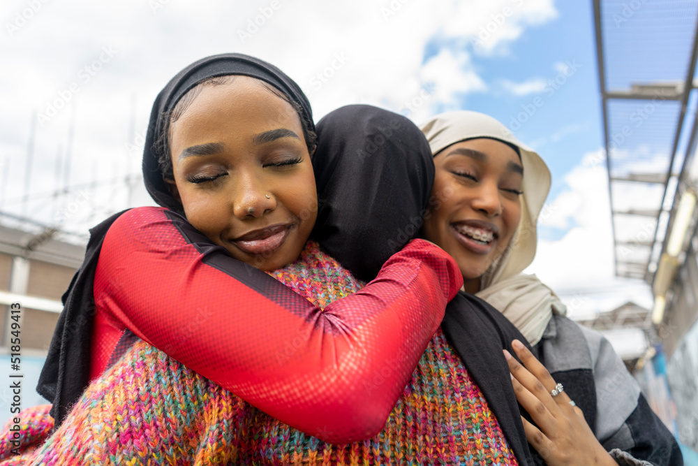 Young women wearing�hijabs�hugging in city - obrazy, fototapety, plakaty 
