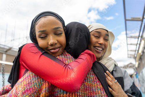 Young women wearing hijabs hugging in city Fototapet
