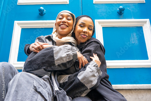 Portrait of two smiling women wearing hijabs embracing in city