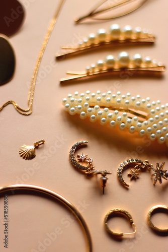 Various gold jewelry and pearl hair clips on peach colored background. Selective focus.