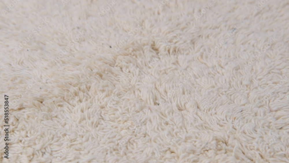 A light-colored carpet with large fibers arranged in random order rotates, close-up. A light-colored carpet with large fibers arranged in random order rotates, close-up.