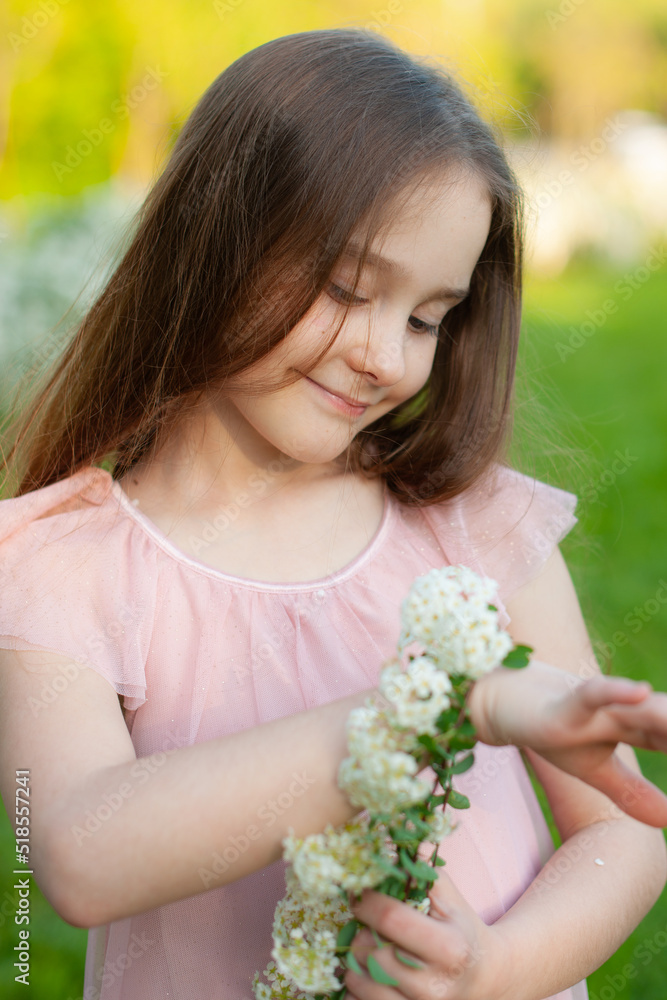 Portrait of a tender girl who admires a bracelet of natural flowers dressed in a pink dress, with loose hair, in the spring park Portrait of a tender girl who admires a bracelet of natural flowers dressed in a pink dress, with loose hair, in the spring park