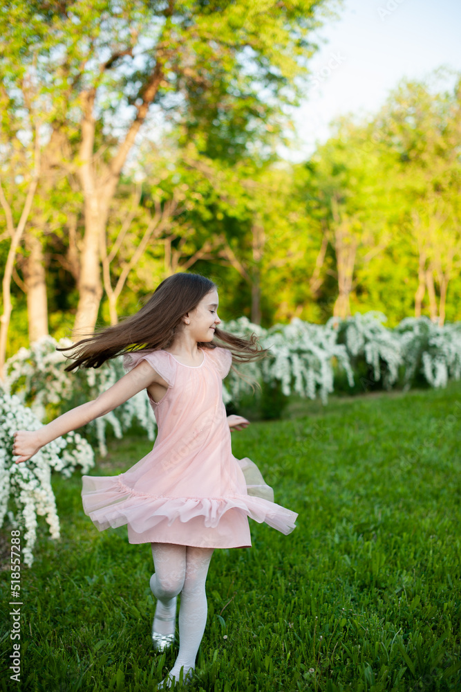Portrait of a tender girl who is spinning with loose hair, dressed in a pink dress, on the meadow in the spring park Portrait of a tender girl who is spinning with loose hair, dressed in a pink dress, on the meadow in the spring park