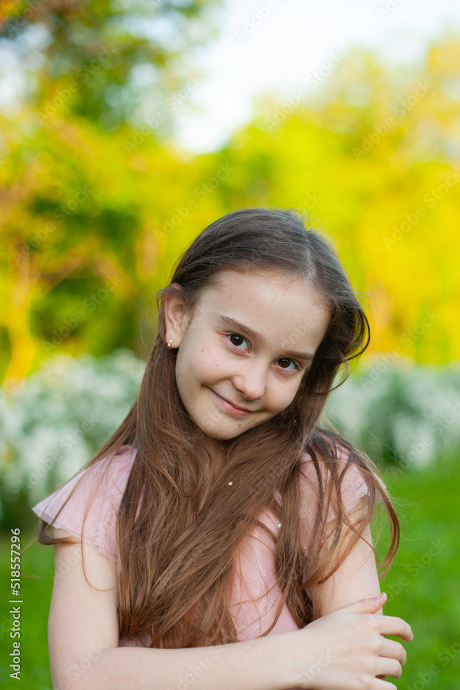 Portrait of a tender girl who looks into the frame and smiles with loose hail, with loose hair, dressed in a pink dress, in the spring park Portrait of a tender girl who looks into the frame and smiles with loose hail, with loose hair, dressed in a pink dress, in the spring park